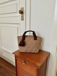 Borsa tote marrone trapuntata con cuciture a onde e nappa su mobile in legno