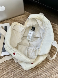 Detailed top view of white quilted heart-shaped tote with red embroidery and zipper