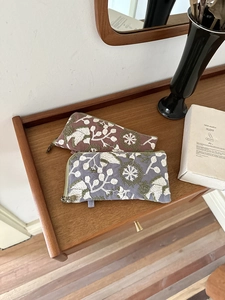 Close-up of embroidered storage bags in tan and grey-blue with floral plant patterns