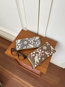 Detailed view of floral bird embroidery on linen zip pouch with glasses on wood surface