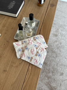 Detail of cream quilted makeup bags with cute cartoon patterns and metal zipper closure