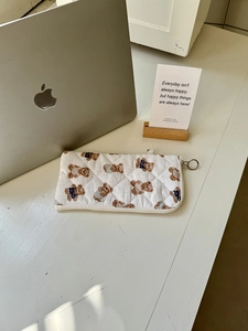 Close-up of quilted white makeup bag with brown bear patterns and metal zipper ring