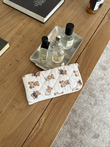 Detailed view of a quilted makeup bag featuring cute teddy bear patterns on a wooden desk