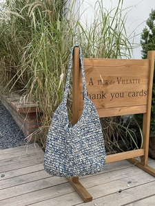 Blue and white woven straw beach bag with wide shoulder strap in a garden setting