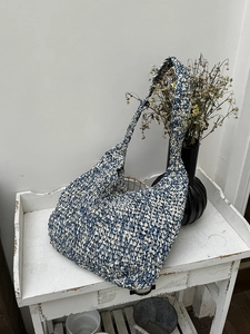 Detail of blue and white woven shoulder bag with wide strap on a rustic shelf