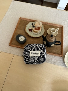 Close-up of black fabric pouch with white embroidery on a rustic wooden tabletop