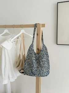 Blue and white woven straw tote bag with integrated shoulder strap on a hanger