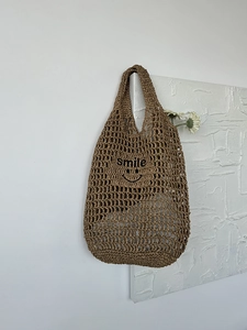 Detail of hollow woven straw bag featuring black smile embroidery on khaki material
