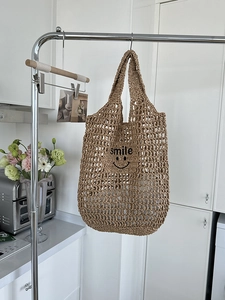 Detail of a brown woven straw tote bag featuring black embroidered smile face and text