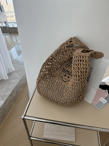 Detail of beige straw tote bag with black smile print on a minimalist metal stand