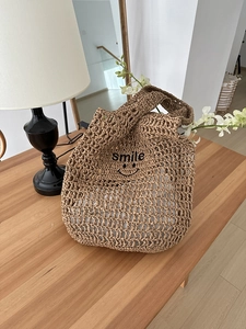 Detail of hollow woven straw shoulder bag featuring black smile embroidery on brown texture