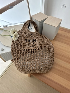 Close-up of brown straw woven tote bag with black smile embroidery on hollow mesh fabric