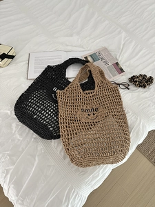 Detail view of woven straw shoulder bags in black and beige with smile print