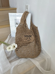 Detail of khaki hollow mesh straw bag with black smile lettering in a lifestyle setting