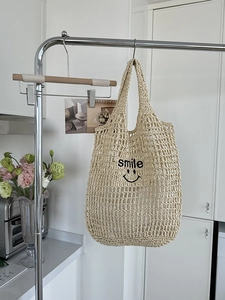 Detail of hand-woven beige mesh bag featuring a black embroidered smile logo for beach use