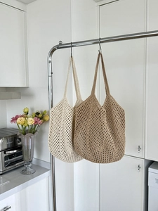 Detail showing two large crochet mesh tote bags in beige and khaki hanging in a kitchen