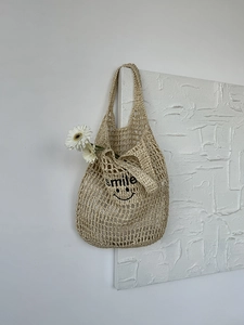 Detail view of the hand-woven hollow net bag featuring a black smile print and mesh texture