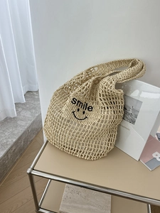 Detail of hand-woven beige straw tote bag featuring a black embroidered smile face and text