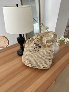 Detail of woven straw tote bag featuring black smile embroidery on mesh pattern