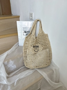 Detail of beige straw mesh tote bag with black smile embroidery on wooden stairs