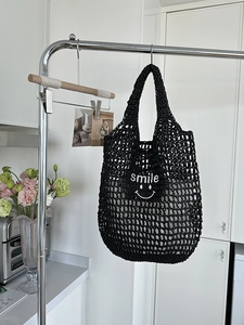 Macro detail of black crochet mesh bag featuring white smile embroidery and woven texture