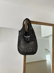 Detail of black hollow woven tote bag with white Smile embroidery and light inner lining