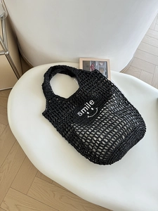Detail of black woven net tote bag featuring a white smile print on white chair