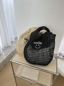 Close-up of hollow straw bag with smile embroidery in black and beige colors