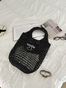 Detail showing black crochet knit net bag with white Smile text and woven handle
