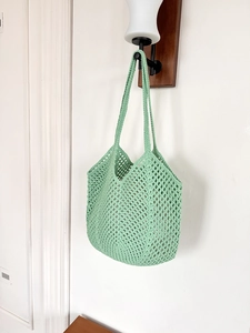 Close-up of light green crochet tote bag with openwork weave hanging on wooden hook