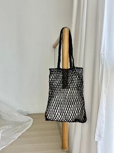 Detail der handgewebten schwarzen Netztasche mit weißem Innenbeutel an Holzstange