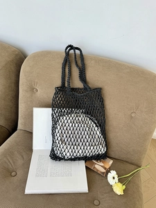 Detail einer schwarzen geflochtenen Netzhandtasche mit Rautenmuster auf einem beigen Sofa