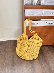 Detailed close-up of yellow hollow crochet tote bag with mesh design on wooden background