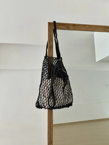 Detail einer schwarzen gewebten Netztsche mit weißem Innenbeutel an einem Holzrahmen