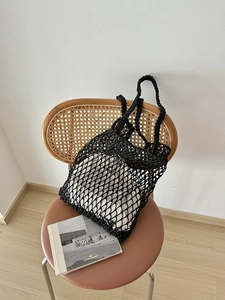 Detail einer schwarzen geflochtenen Netztasche mit beigem Innenfutter auf einem Stuhl