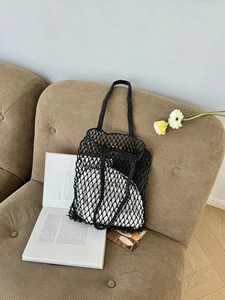 Detail einer schwarzen geflochtenen Netz-Schultertasche auf einem Sofa mit Buch