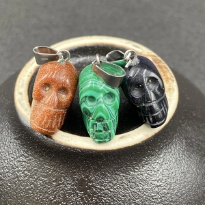 Vue détaillée de trois pendentifs tête de mort en pierre de soleil, malachite et grès bleu