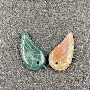 Detailed view of carved stone angel wing pendants in green and orange with drill holes