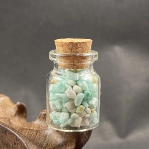 Close-up of small glass bottle with light blue crystals on dark wooden stand