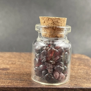 Close-up of a small glass bottle filled with natural dark red garnet crystal stones