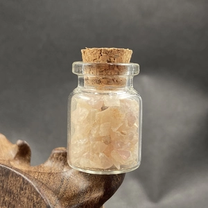 Macro detail of a clear mini glass jar with pink crystal stones on a dark wood stand
