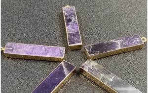 Makroansicht von fünf rechteckigen Amethyst-Anhängern mit vergoldetem Rand auf dunklem Grund