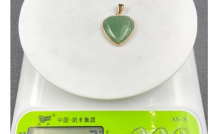 Macro del ciondolo a cuore verde con bordo dorato su bilancia digitale per il peso