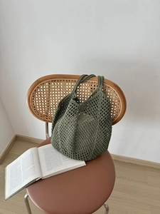 Detail of dark green hollow crochet shoulder bag resting on a rattan chair with an open book