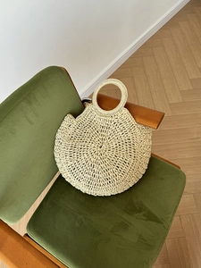 Dettaglio di una borsa rotonda in paglia beige su una sedia di velluto verde elegante