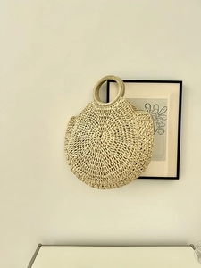 Dettaglio di borsa minimalista in paglia con manici circolari e trama intrecciata naturale