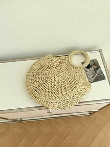 Dettaglio della borsa a mano minimalista in paglia beige con design a manico rotondo