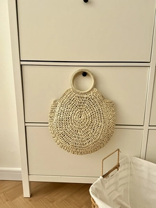 Dettaglio di una borsa rotonda in paglia intrecciata appesa a una maniglia in stanza