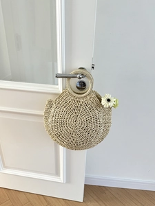 Dettaglio di borsa rotonda in paglia intrecciata beige con manici circolari su una porta