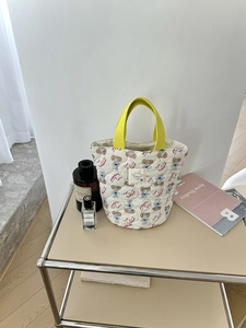 Gros plan d'un sac seau matelassé blanc avec anses jaunes sur un support minimaliste